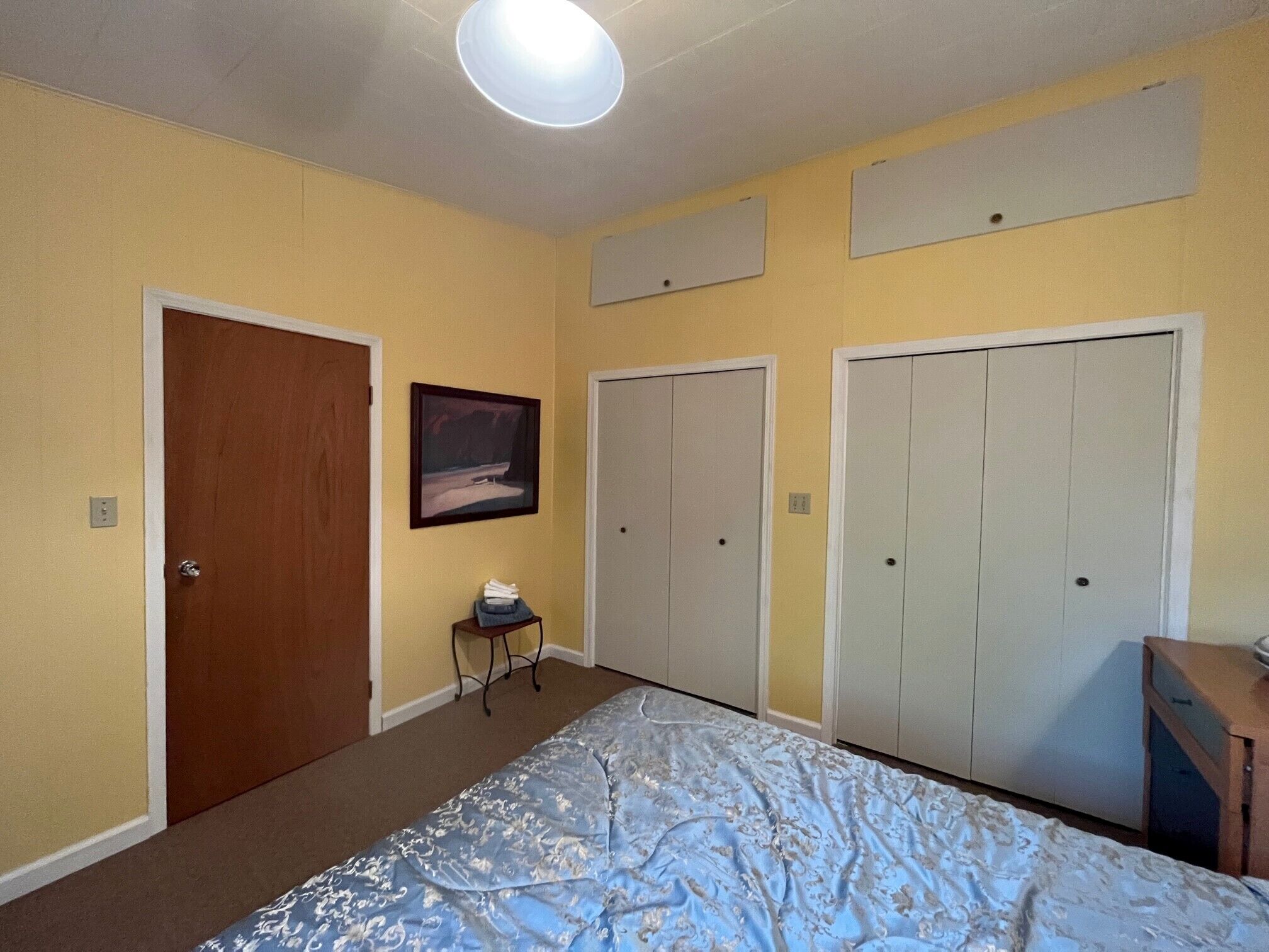 Ein Schlafzimmer mit einem Bett, einer Holztür, einem kleinen Tisch mit einem Handtuch und drei weißen Schränken.