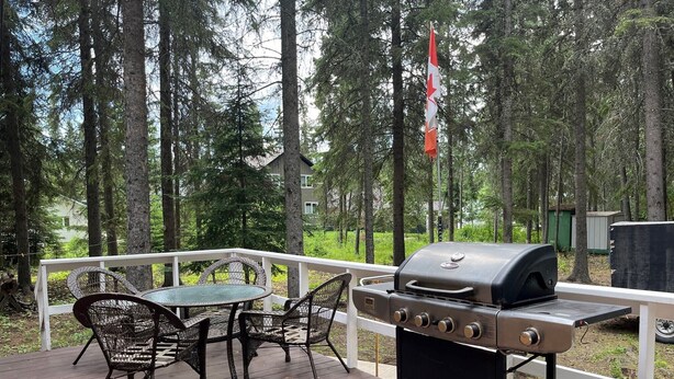 Een terras buiten met een barbecue, rieten stoelen en een tafel.