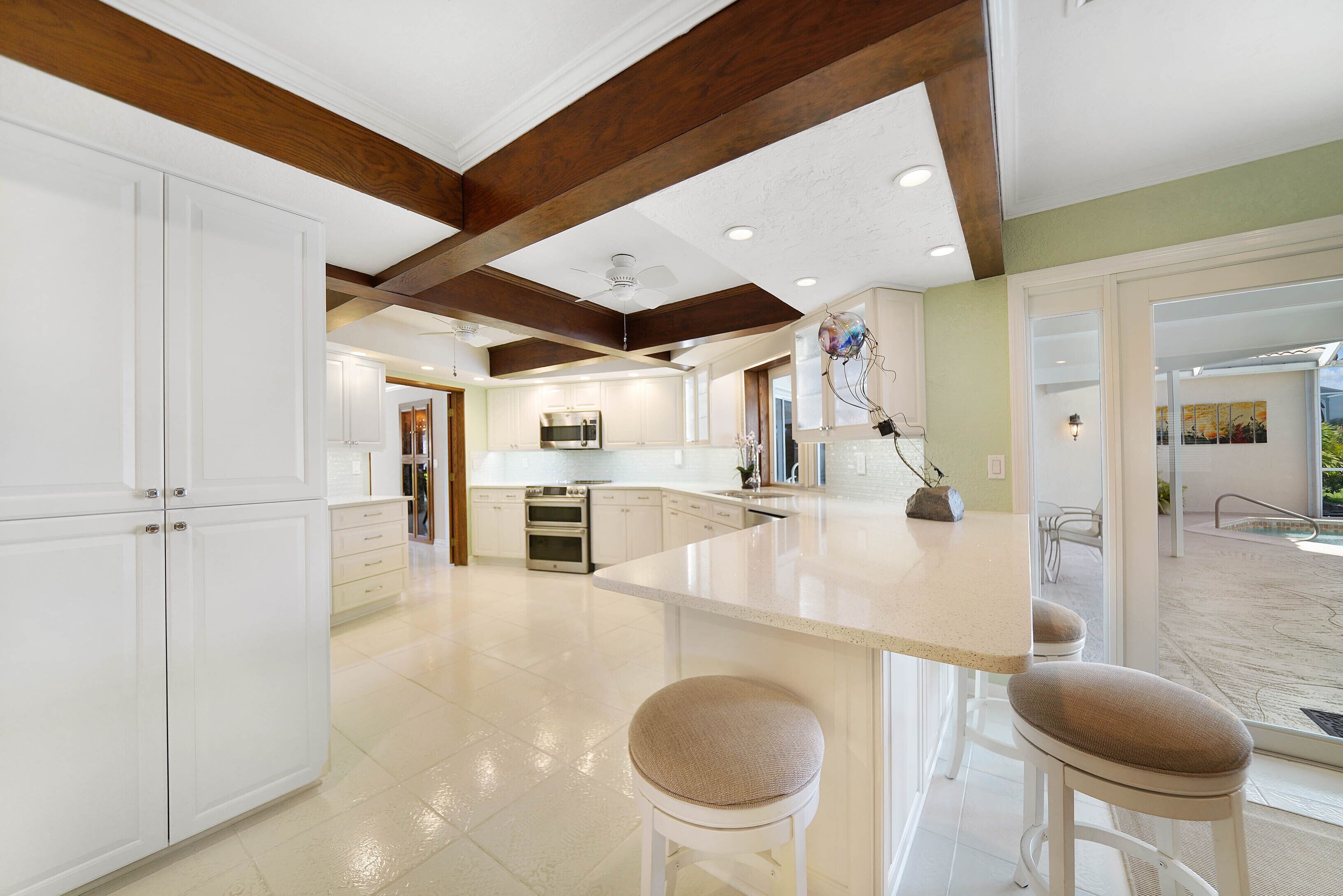 A spacious kitchen with white cabinets, a large island with bar stools, and a view to the outdoor patio.