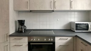 Cuina amb armaris de colors clares, taulell negre, cafetera, microones i forn.