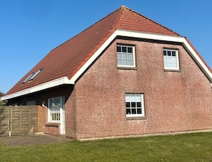 Une maison en briques rouges, avec un toit à forte pente, deux fenêtres et un portail en bois.