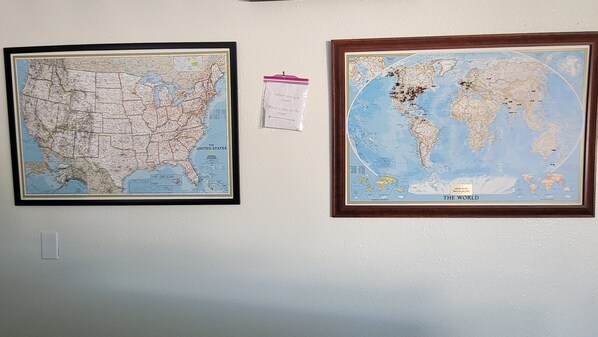 Two framed maps on a wall, one of the United States and one of the world, with a small instruction card between them.