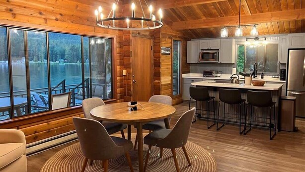 A modern kitchen with a central island, large windows, and a dining area with a round table and chairs.