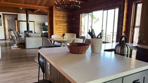 A modern kitchen with a large island, wooden cabinetry, and a hanging light fixture.
