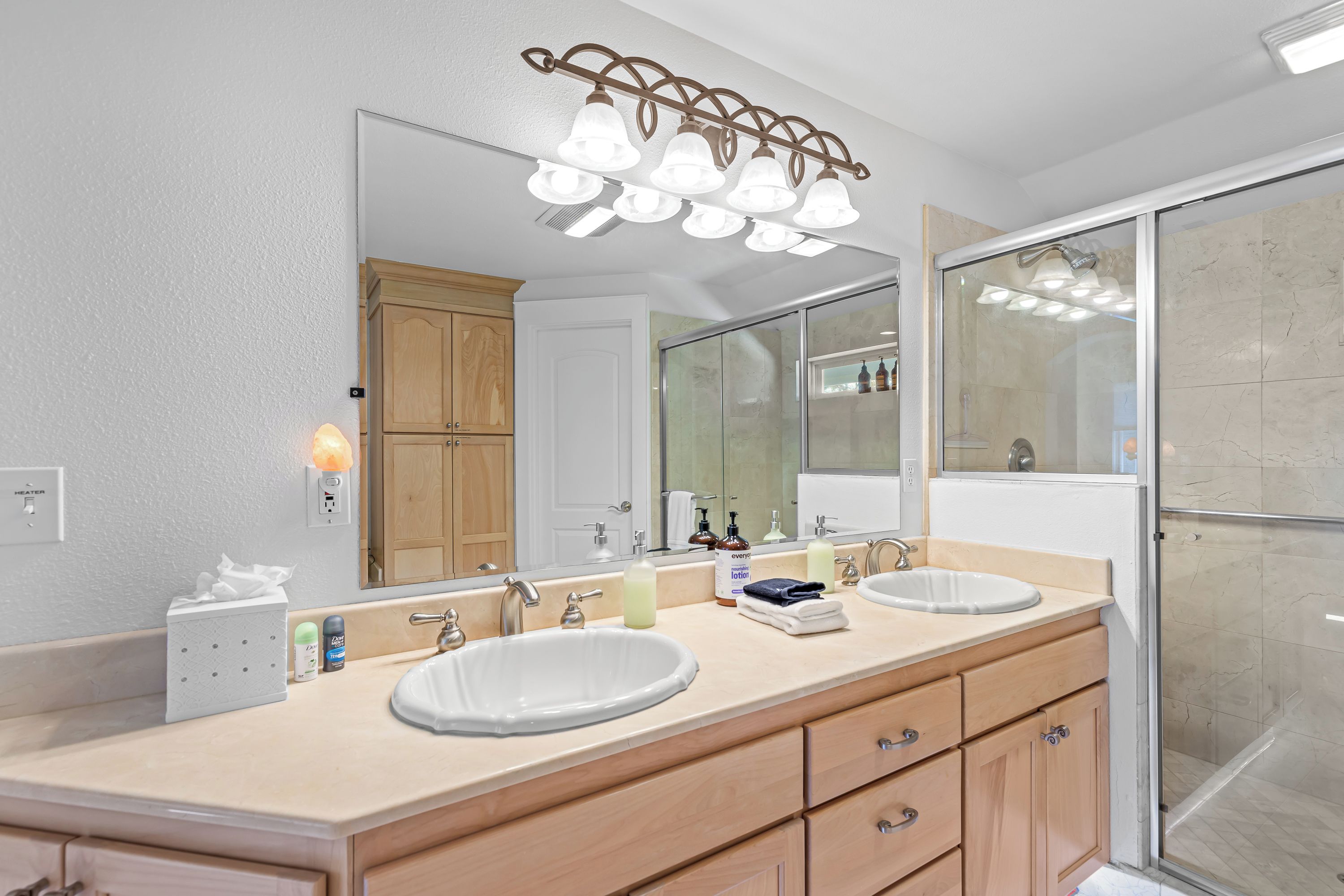 A bathroom with a double sink vanity, a large mirror, a shower enclosure, and a heater on the wall.