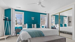 Een moderne slaapkamer met een groot bed, een bankje, een kledingkast en een plafondventilator.