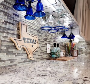 A kitchen with a Texas state sign, blue hanging lights, and a coffee station.