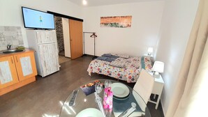 A compact hotel room with a bed, a small table with a glass top, a TV, a wardrobe, and a door leading to a bathroom. - Studio in Gale Albufeira (Albufeira)