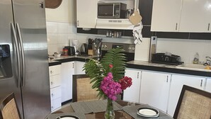 Una cucina moderna con mobili bianchi, elettrodomestici in acciaio inossidabile e un tavolo da pranzo per quattro persone con sedie in rattan.