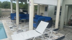 Un'area lounge esterna coperta con divani blu e una poltrona bianca, una piscina e un cartello che indica il divieto di fumare.