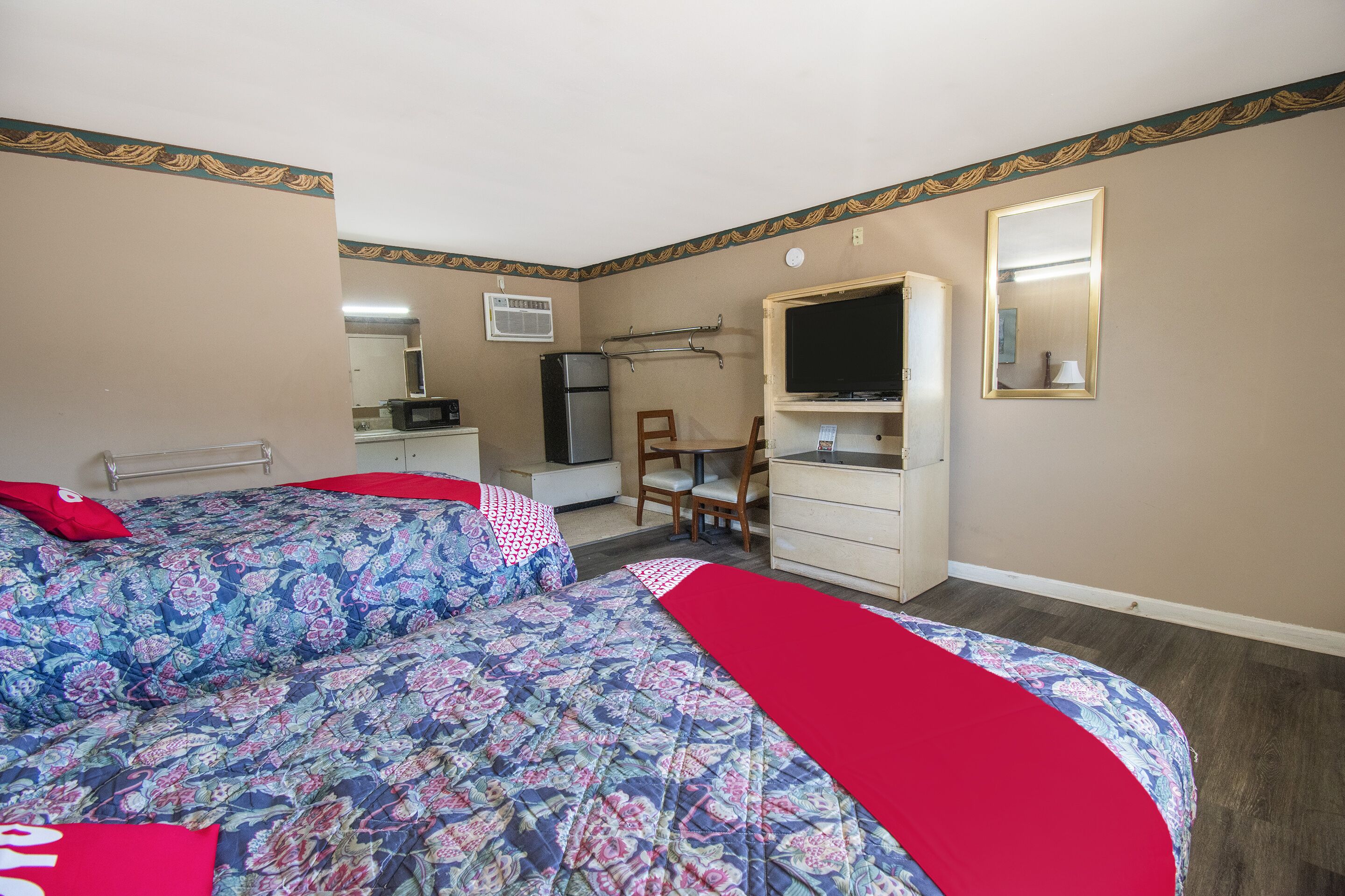 A hotel room with two beds, a desk, a chair, a television, and a dresser.
