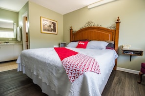 A neatly made bed with a white and red patterned blanket, a wooden headboard, and a small bedside table with a telephone.
