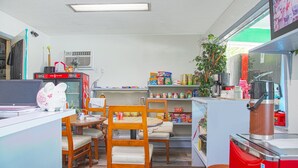 A compact kitchen with wooden chairs, a refrigerator, and shelves stocked with various food items. - OYO Hotel Calhoun, GA I-75 (Calhoun)