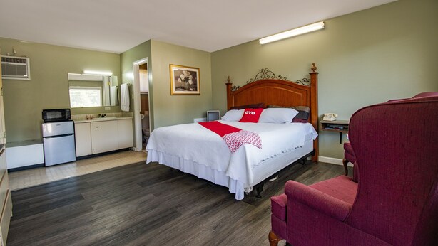 A hotel room with a bed, a red chair, a kitchenette, and a bathroom. - OYO Hotel Calhoun, GA I-75 (Calhoun)