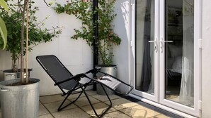 Une terrasse avec une chaise pliante, des plantes en pot et une porte-fenêtre coulissante donnant sur une pièce.