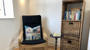 Une chaise avec un coussin patchwork, une petite table avec un livre et une bibliothèque remplie de livres et de paniers en osier.