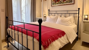 Un lit bien fait, recouvert d’une couvre-lit rouge et blanche, avec un cadre en métal noir et des oreillers blancs. Un tableau représentant des fleurs est accroché au mur au-dessus du lit.