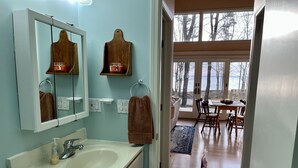 Een badkamer met een wastafel, spiegel, handdoekhouder en uitzicht op een eetruimte door een open deur.