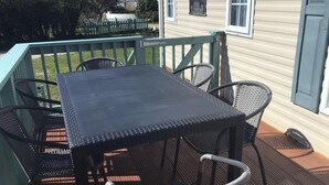 Une terrasse avec une table et des chaises, une clôture en bois et une maison en arrière-plan.