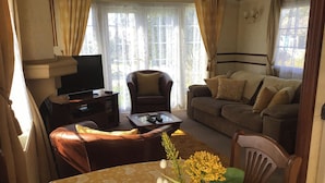 Un salon avec un canapé, un fauteuil et une table recouverte d’une nappe à motifs floraux.
