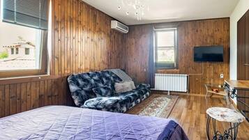Een kamer met houten wanden, een bed met een paars sprei, een bank met een zachte hoes, een aan de muur bevestigde televisie en een radiator.
