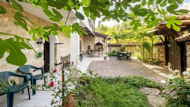A stone courtyard with outdoor seating, a brick oven, and lush greenery.