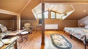 A cozy attic bedroom with wooden walls, a large bed, a chair, a desk, and a radiator.
