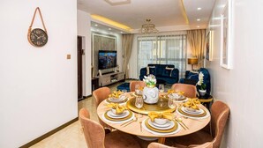 A modern dining room with a round table set for four, a television in the background, and a blue sofa in the living area. - Modern 3-Bed Apartment in the heart of Nairobi (Nairobi)