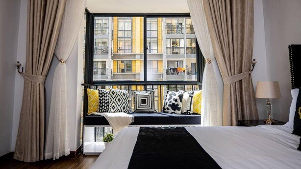 A bedroom with a large bed, a window seat with cushions, and curtains. - Modern 3-Bed Apartment in the heart of Nairobi (Nairobi)
