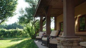 Une terrasse couverte avec deux fauteuils en osier et un pilier en pierre.