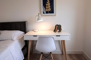 Quarto bem organizado com uma cama, uma escrivaninha com abajur e uma cadeira.