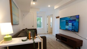 Un salon moderne avec un téléviseur à écran plat fixé au mur, un canapé, une table basse et une lampe.