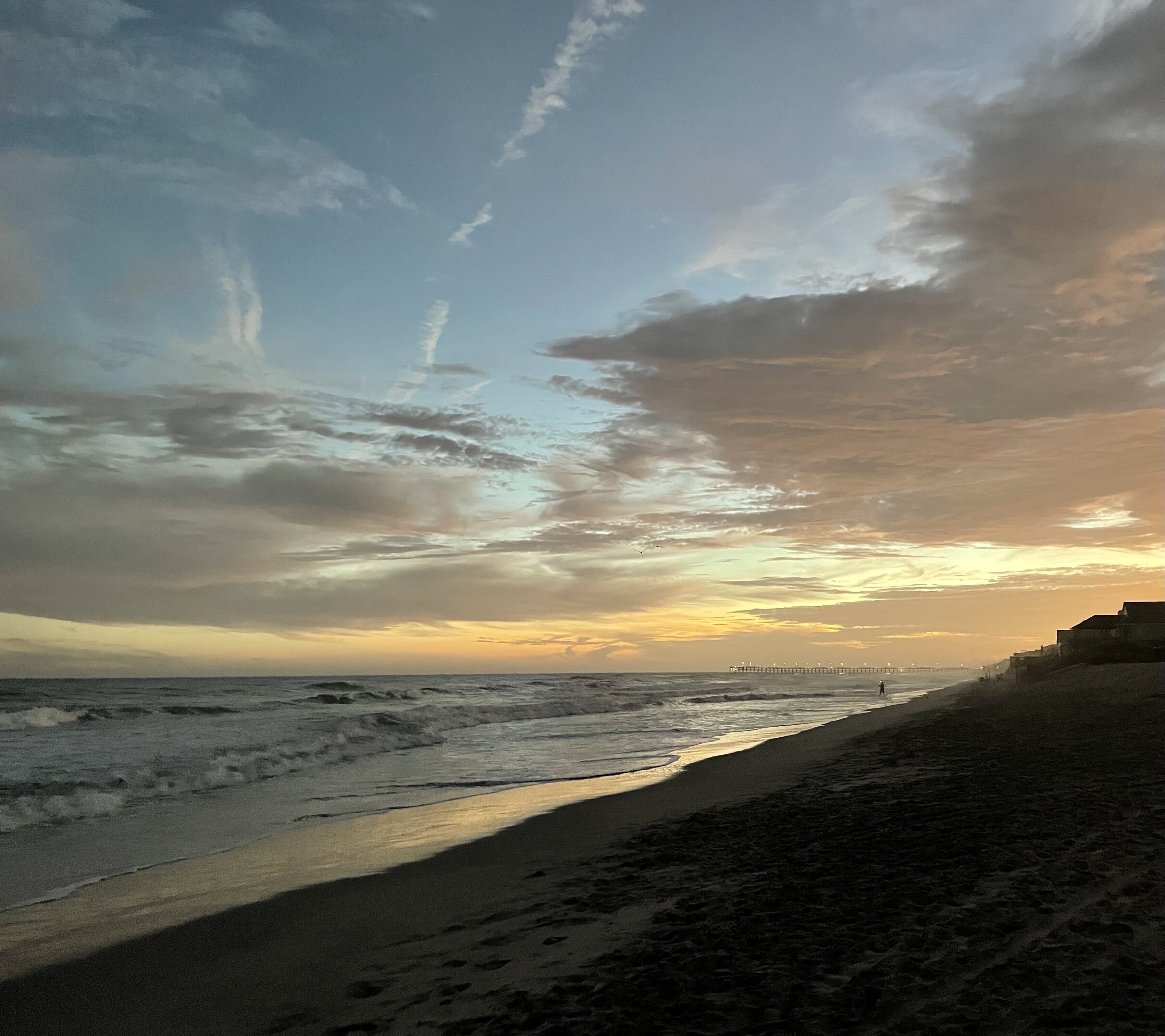 Una spiaggia con un molo che si protende sull'oceano, una riva sabbiosa e un cielo nuvoloso.