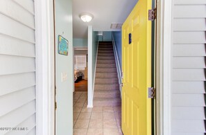 Un pasillo con una puerta amarilla, una escalera y una habitación con cama.