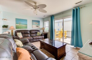 Relax in the living room with a comfortable sofa, coffee table, and ceiling fan, offering a view of the deck area.