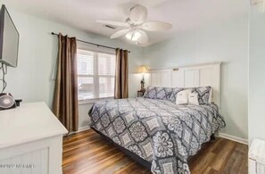 A bedroom with a bed, a ceiling fan, a window with curtains, and a bedside table with a lamp.