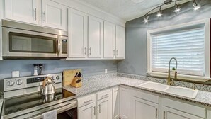 A kitchen with white cabinets, a stainless steel microwave, a stove, and a sink.