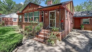 A brick house with a front porch, steps, and potted plants.