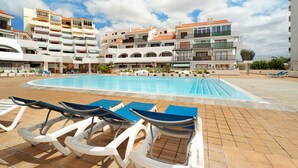 Una piscina con sillas de descanso, un solárium empedrado y edificios de varios pisos al fondo.