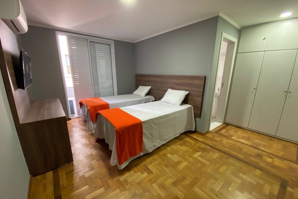 A hotel room with two beds, a wooden floor, a wardrobe, and a TV.