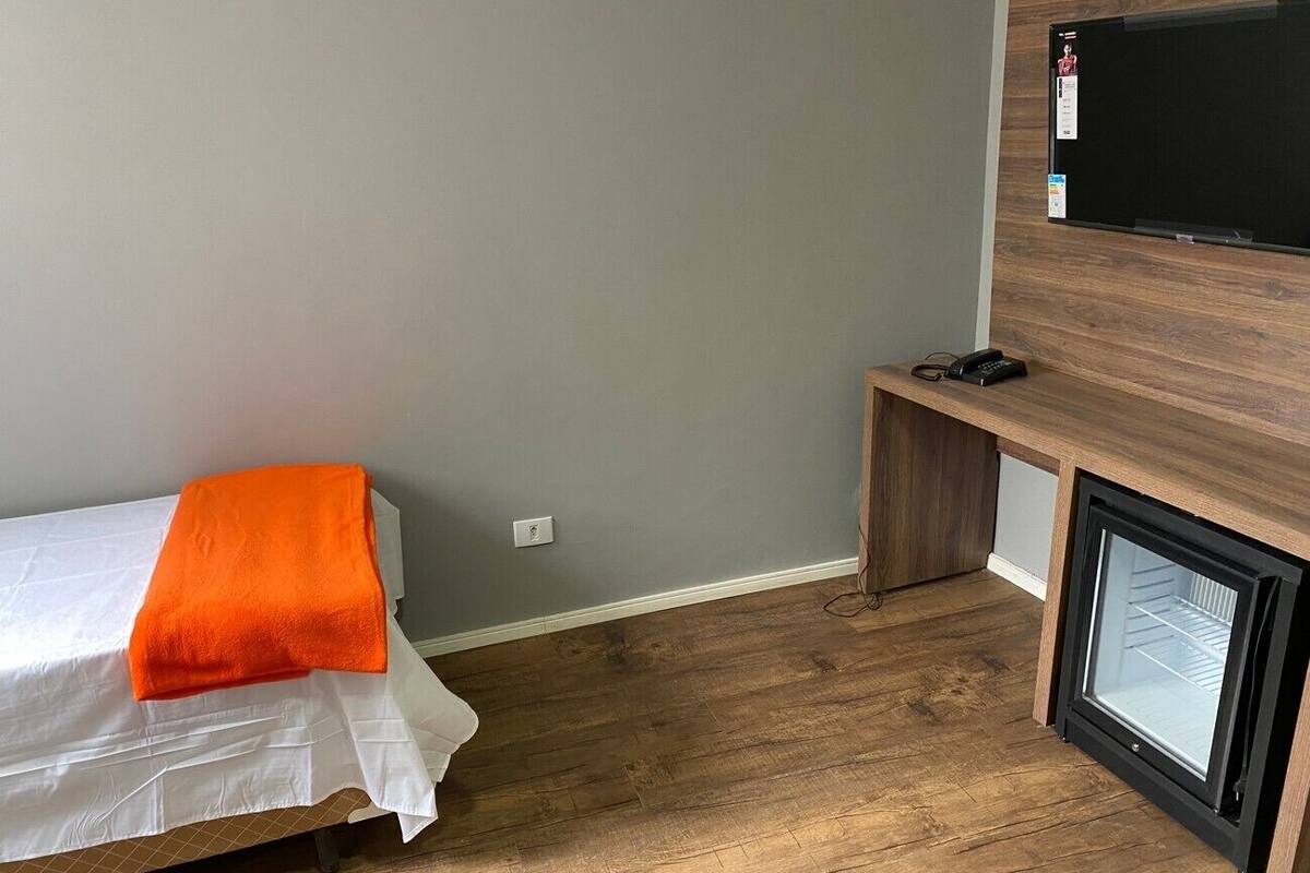 A small room with a bed, a television mounted on the wall, and a small seating area.