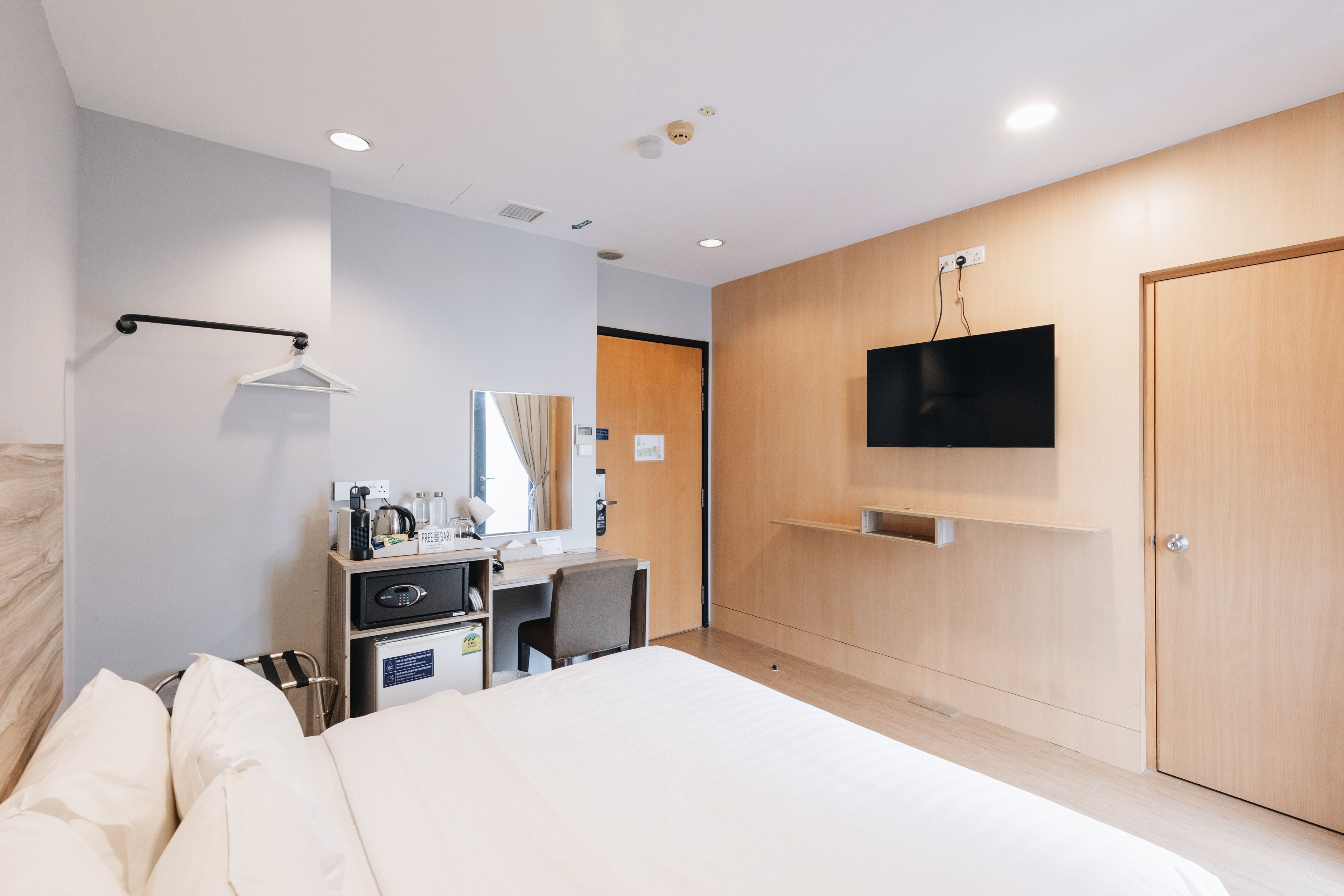 A hotel room with a bed, a desk with a chair, a TV mounted on the wall, and a wardrobe.