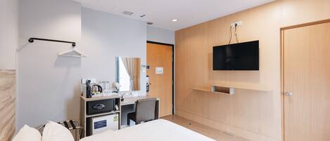 A hotel room with a bed, a desk with a chair, a TV mounted on the wall, and a wardrobe.