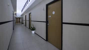 A long, narrow hallway with doors on one side, potted plants, and a tiled floor.