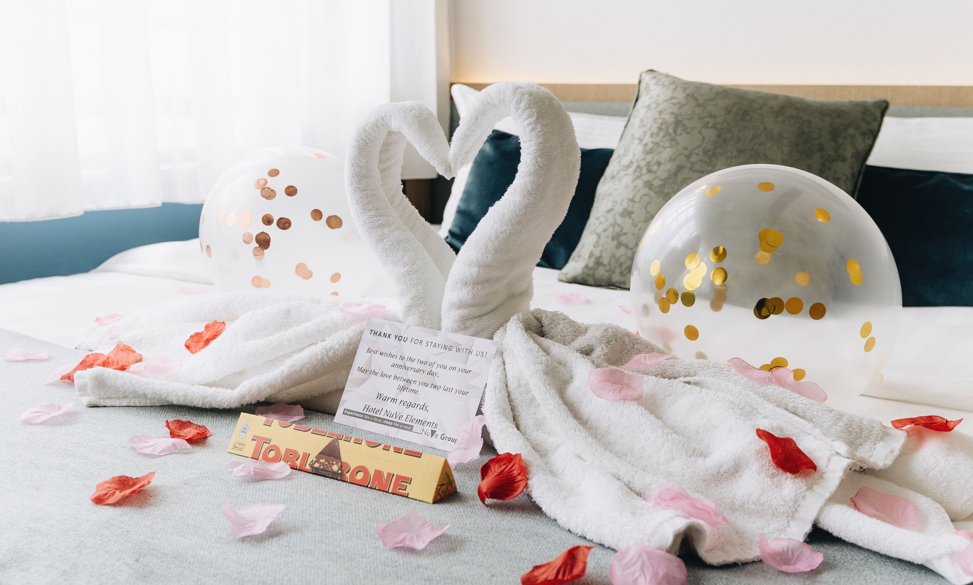Een bed met een handdoek in de vorm van een zwaan, een bedankkaartje en een chocoladereep.