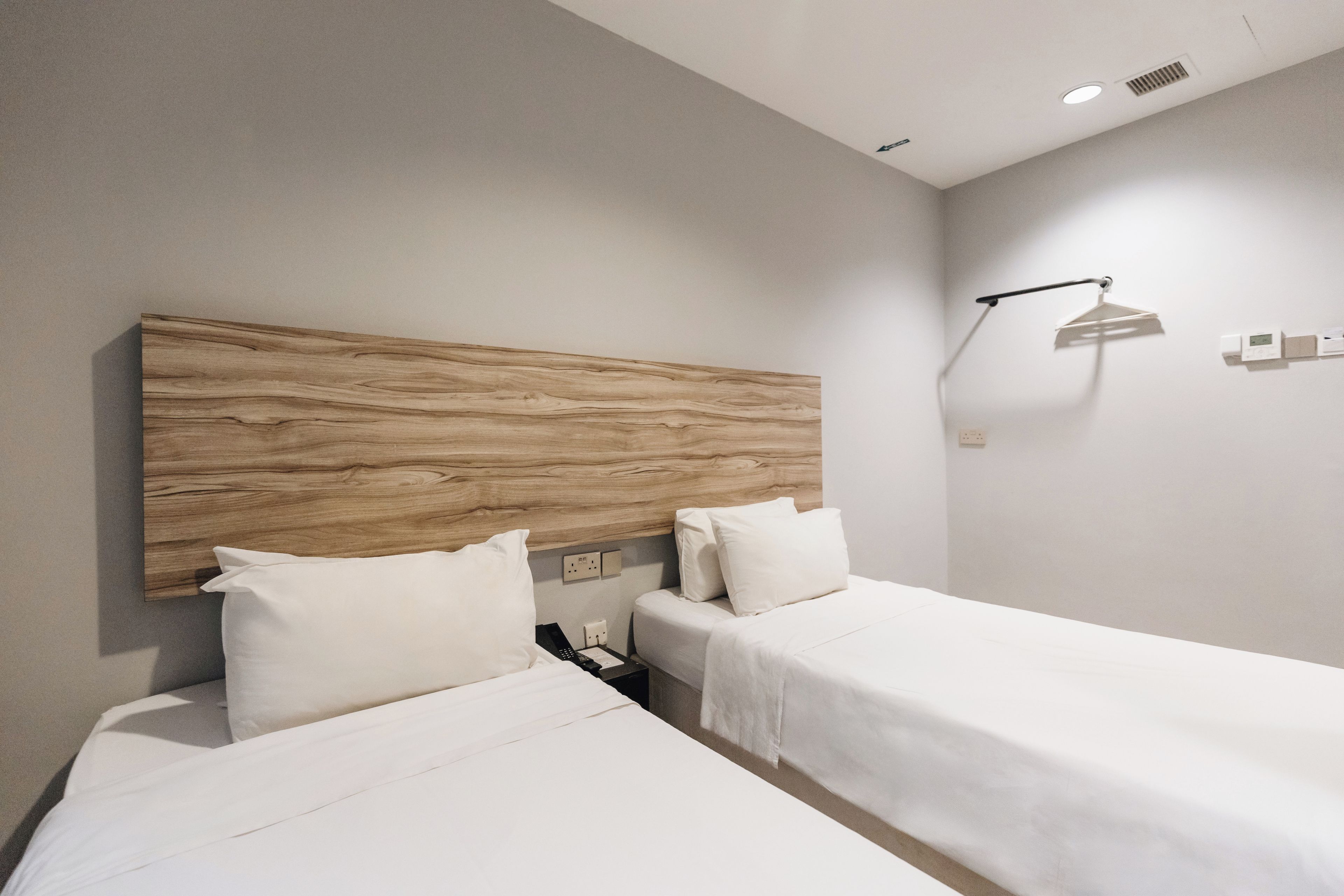 Habitación de hotel con dos camas, cabecero de madera, mesita de noche con teléfono y lámpara de pared.