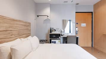 Habitación de hotel con una cama grande, un escritorio con espejo, un refrigerador pequeño y un armario de madera.