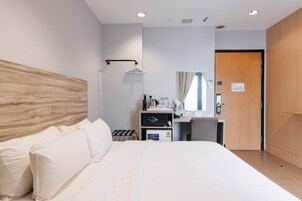 Habitación de hotel con una cama grande, un escritorio con espejo, un refrigerador pequeño y un armario de madera.