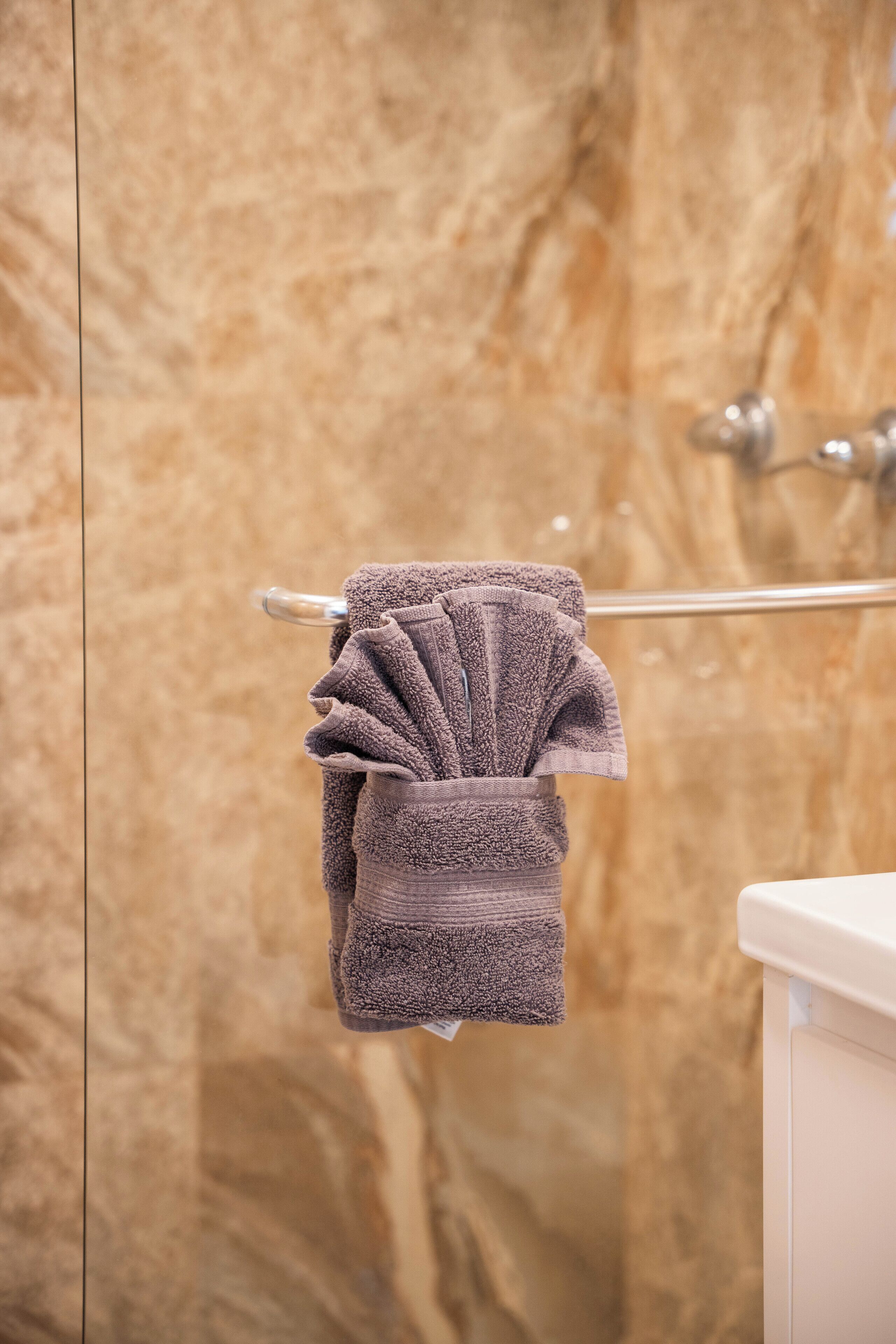 A bathroom with a marble wall, a towel rack with a folded towel, and a white sink.