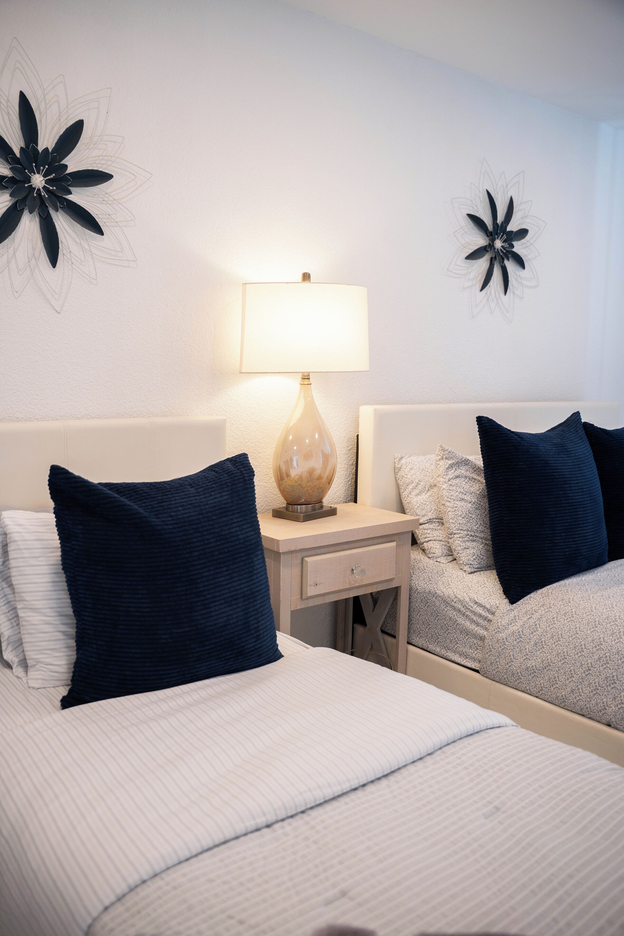 A hotel room with two beds, a nightstand with a lamp, and wall art.